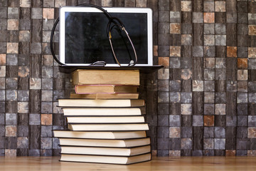 Work place table with stacks of real books on it and modern lap top and Stethoscope 