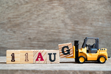 Toy forklift hold block G to complete word 11 aug on wood background (Concept for calendar date in month August)