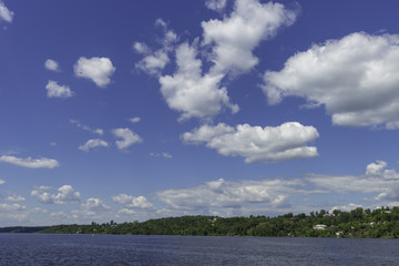 Summer countryside with a river, white clouds against a blue sky. On the banks are different villages and houses.
