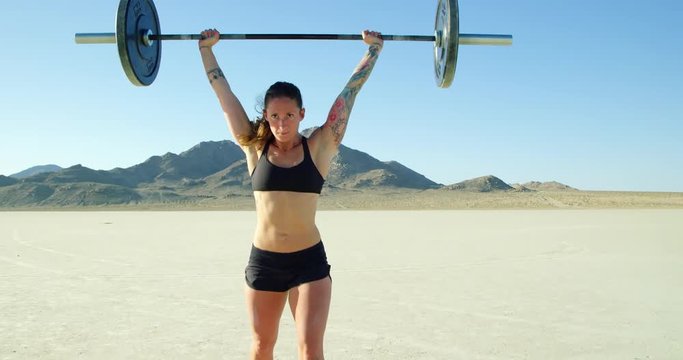 Athletic woman lifting olympic barbell in desert lifting weight crossfit work out