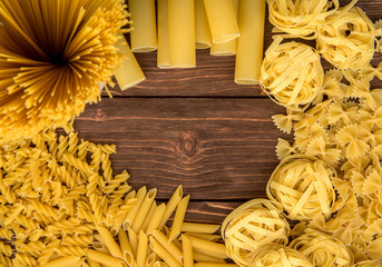 Paste theme. Different kinds of pasta on a wooden background. Farfalle, fettuccine, noodles, fusilli and penne rigate