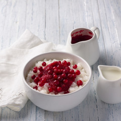 Rice pudding with cranberry jam and fresh cranberries in a white bowl on a light blue background, selective focus. Delicious traditional breakfast
