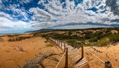 View of sand dunes on the Guincho beach near Atlantic coast. Landscape of sunny day, blue sky and a mountain in background. Cascais. Portugal. - obrazy, fototapety, plakaty