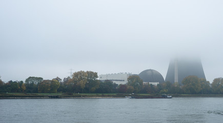 Fototapeta premium Foggy autumn morning in Germany on the river Rhine, a flowing barge. Visible chimney of a nuclear power plant in the fog.