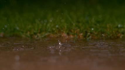 DOF: Crystal clear raindrops falling into murky puddle create a beautiful ripple