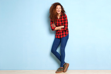 Full body happy young woman leaning against blue wall