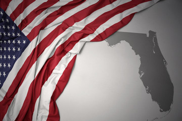 waving national flag of united states of america on a gray florida state map background.