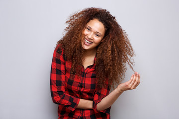 cheerful young woman smiling against gray background with hand in curly hair