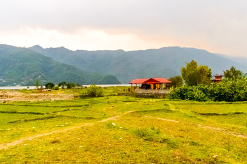 Photograph of winter season: A farm house, lake, mountain, clear sky and farm land. Wide angle landscape of Pokhara Lake at Kathmandu Nepal. Vintage film look. Vacation Freedom, Simplicity Concept.
