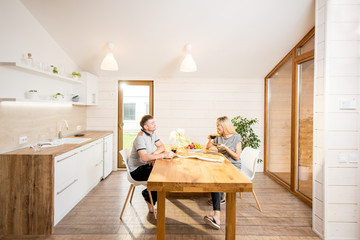 Young and happy couple having a breakfast sitting at the wooden table of the dining room of the...