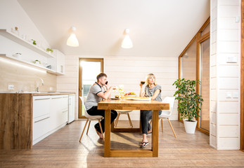 Young couple having a breakfast sitting at the wooden table of the dining room of the modern country house. Wide angle view
