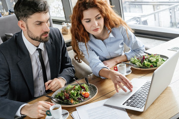 Businesspeople having business lunch at restaurant sitting eating salad drinking coffee browsing laptop concentrated