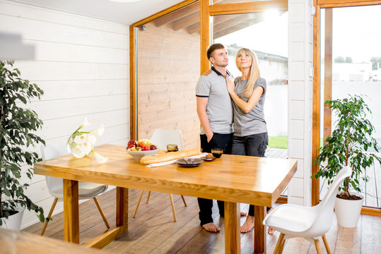 Portrait of a young and happy couple standing together in the cozy interior of the modern wooden house