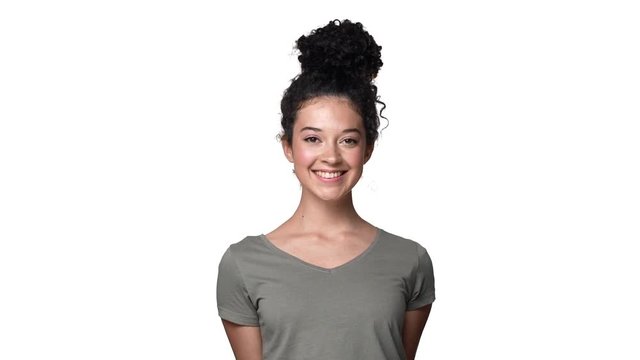 Portrait of gorgeous caucasian woman with long dark hair tied in bun looking at camera with beautiful smile, isolated over white background in studio slow motion. Concept of emotions