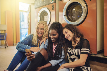 Girlfriends sitting together at the laundromat using a cellphone