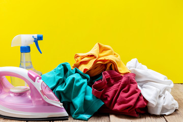 iron and stack of colored clothes on yellow background.