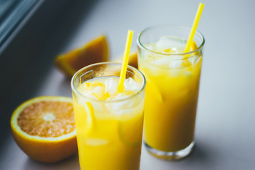 Glasses of fresh orange juice with ice and orange slices on a white background.