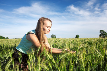 Beautiful long-haired woman in the field watching the growing corn during the sunrise © charmphoto