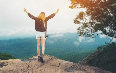 Happy female hiking with camera on the high cliffs at sunrise