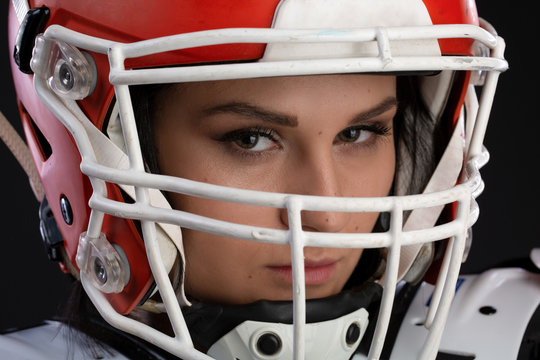 Portrait of sexy attractive young girl with a bright make-up in a sports outfit for rugby with the helmet on head strongly looking forward standing on a black background