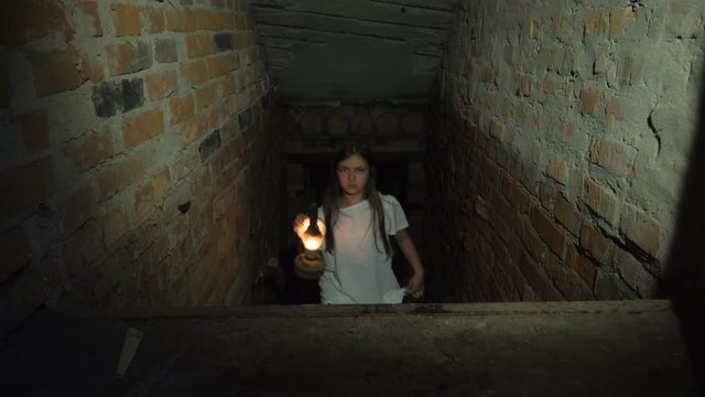 A little girl climbs up the steps from the dark cellar lighting her way with a kerosene lamp
