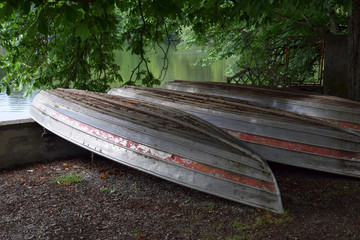 scruffy row boats lying upside down on the shore of a lake, neglected old and rotten rowboat upside down made of metal and wood