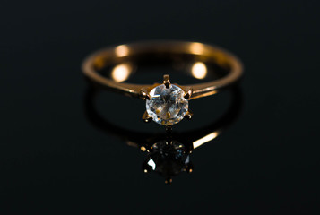 Real gold ring with diamond reflecting on black shiny surface close up macro shot.