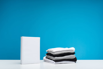 Close up of pile of clean black and white t-shirts lying on wooden surface. Packet of washing...