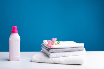 Exquisite fragrance. Pile of washed and softened towels with pink flower on top. Can of plasticizer standing nearby