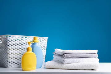 Close up of clean bath towels lying on white table by clothesbasket and detergents. Washing is easy with properly selected means