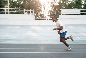 Fototapeta premium Movement is life. Full length side view happy man making workout on open air in stadium. He flourishing arms. Copy space
