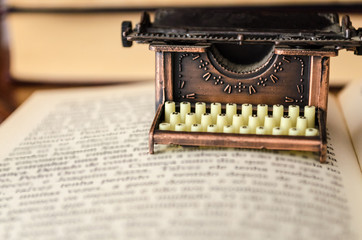 Small typewriter in copper tones over a page of a book. Decoration item. Concept of reading, writing, old times, past. Close up. Blurred background.