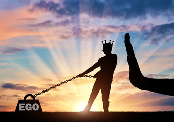 The silhouette of a selfish man with a crown on his head draws a heavy load - the ego and a large...