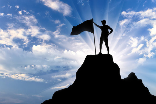 Silhouette Of A Climber With A Flag On Top Of A Mountain.