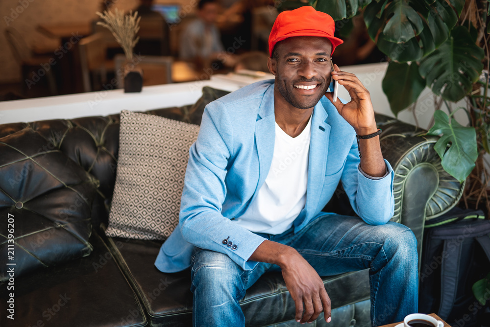 Poster portrait of beaming man speaking by phone while resting on comfortable couch
