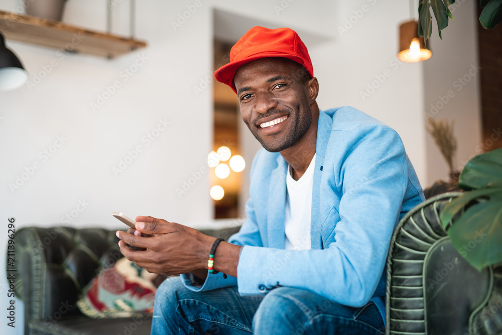 Aufkleber portrait of beaming man using phone while resting on comfortable couch in apartment
