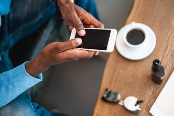 Close up man hands typing in modern phone opposite table with cup of coffee. Top view