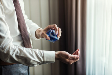Handsome guy is choosing perfumes, Elegant man in suit using cologne,groom getting ready in the morning before wedding ceremony