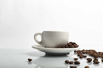 Tazza di caffè bianca con chicchi con un leggero riflesso