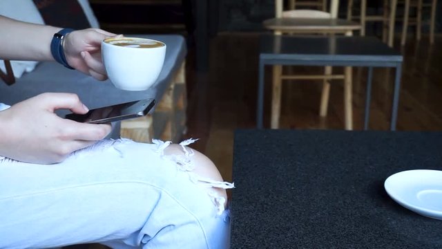 Female student messaging and drinking coffee in city cafe during her break. Young girl drinking coffee and relaxing alone in the morning.