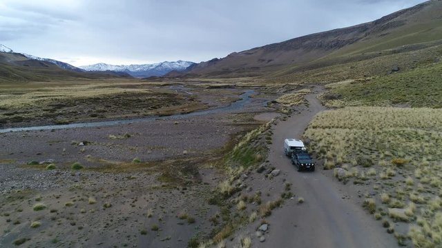 Aerial drone scene of The Andes mountains, in Mendoza, Cuyo Argentina. Patagonia steppe landscape. Camera going backwards over a gravel lonely road tracking van with trailer, motorhome.