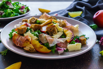 fresh salad of lettuce leaves, pieces of jamon, pieces of crackers and pieces of caramelized peaches and pieces of cheese on the table