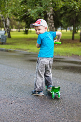 a little boy in a cap on his green scooter riding in a pack