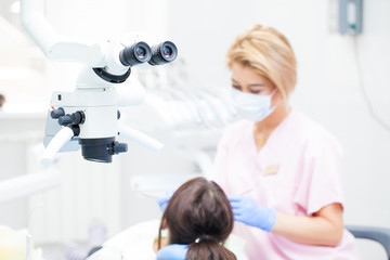 Professional dental endodontic binocular microscope in the treatment room. Against the backdrop of a female dentist and a female patient. Focusing on a microscope