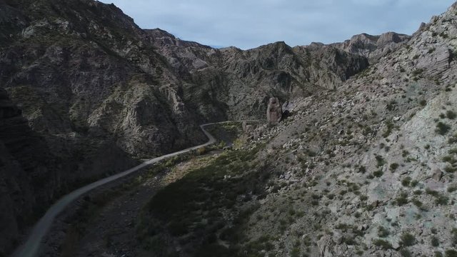 Aerial drone scene of Atuel river canyon in San Rafael, Mendoza, Cuyo Argentina. Camera moving forwards towards big rocks. Gravel street next to green plants and river. Colorfull rocks.