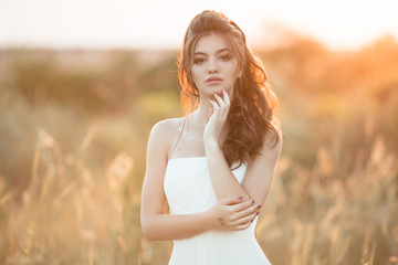 Fototapeta na wymiar Portrait of beautiful young bride in field over sunset lights
