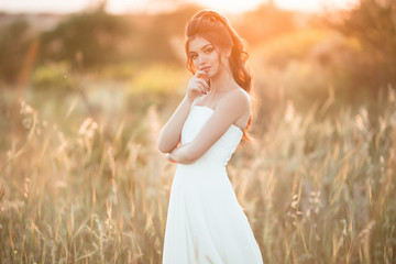 Fototapeta na wymiar Portrait of beautiful young bride in field over sunset lights