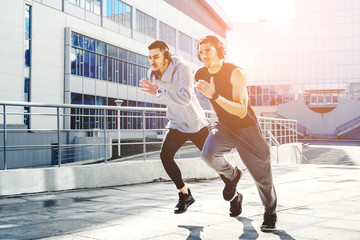 Obraz premium Two friends on a morning run. Young athletes involved in sports in the city. The sun's beam hits the frame. The photo represents a healthy lifestyle and sport.