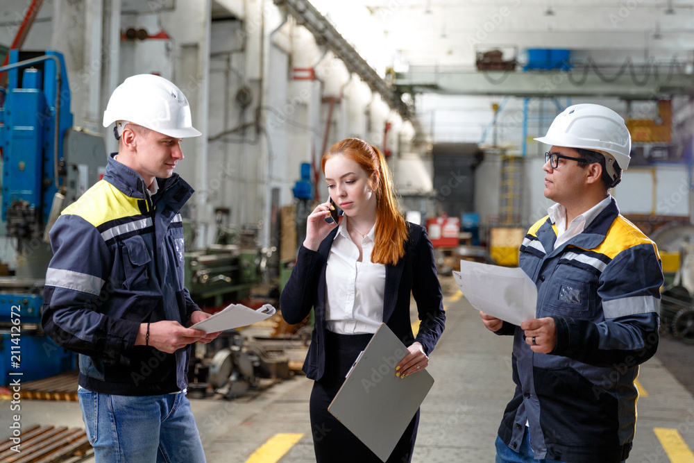 Poster young successful engineers are discussing the technical documentation. engineers at the factory in w