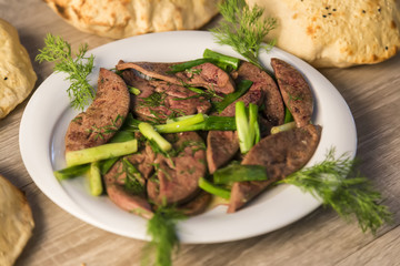 lamb liver food with green vegetables in the plate and local bread on the wooden table for restaurant and kitchen concept.